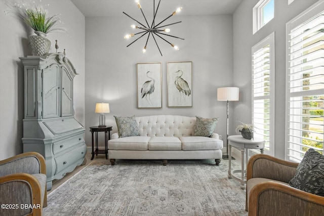 living area with an inviting chandelier, baseboards, light wood-style flooring, and a towering ceiling