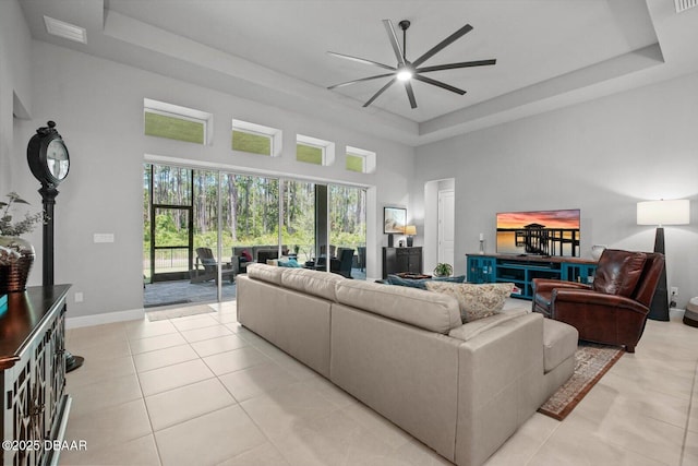 living area featuring light tile patterned floors, ceiling fan, a tray ceiling, and a towering ceiling