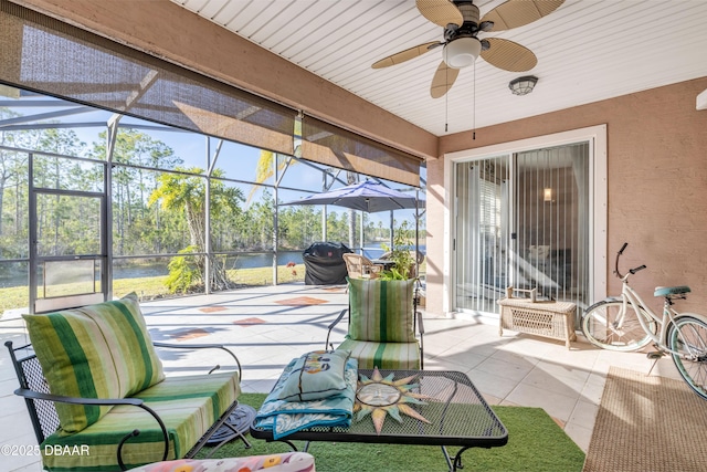 view of patio featuring grilling area, ceiling fan, a water view, and glass enclosure