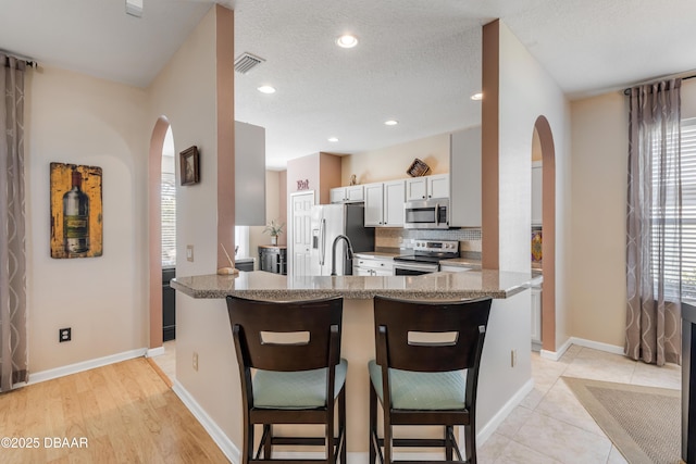 kitchen featuring a kitchen bar, plenty of natural light, kitchen peninsula, stainless steel appliances, and white cabinets