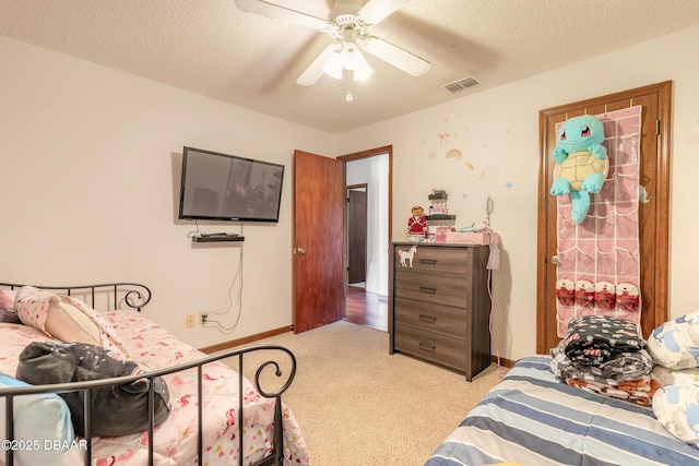 bedroom with a textured ceiling, visible vents, a ceiling fan, and light colored carpet