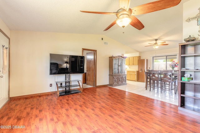 living area featuring vaulted ceiling, visible vents, light wood-type flooring, baseboards, and ceiling fan