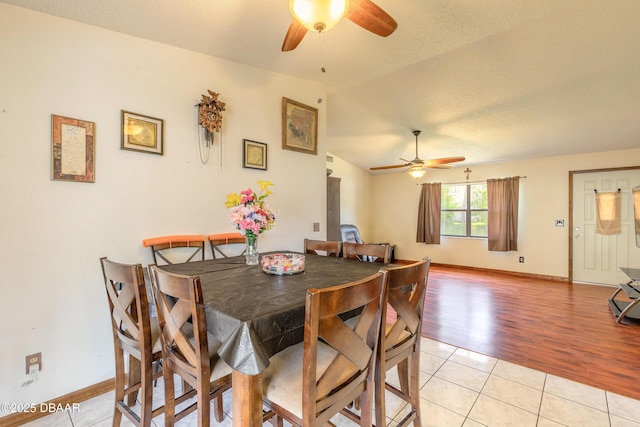 dining area featuring vaulted ceiling, a textured ceiling, light tile patterned flooring, ceiling fan, and baseboards