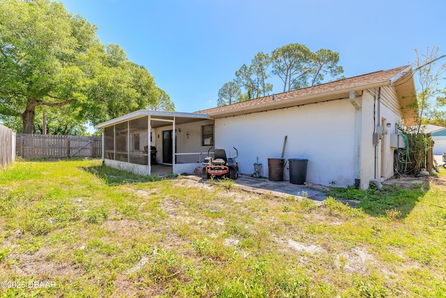 rear view of house with stucco siding, a sunroom, a fenced backyard, and a lawn