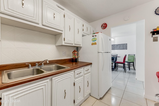 kitchen with white refrigerator, sink, light tile patterned floors, and white cabinets