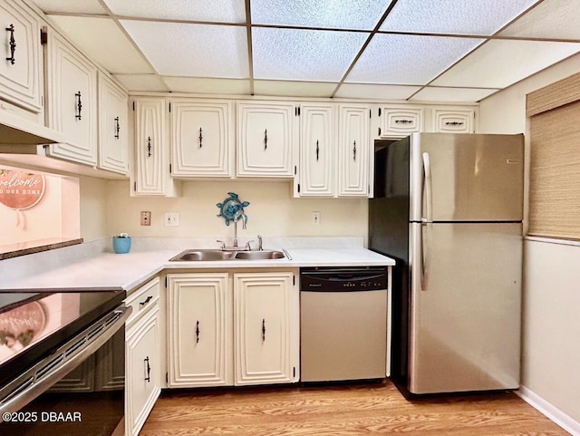 kitchen featuring sink, appliances with stainless steel finishes, white cabinets, a drop ceiling, and light wood-type flooring