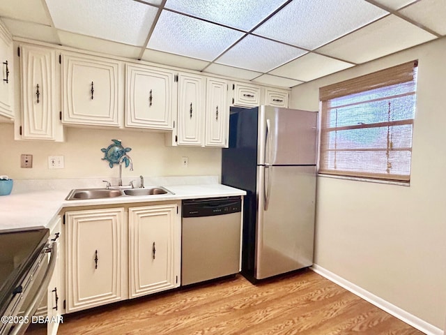 kitchen featuring appliances with stainless steel finishes, sink, white cabinets, a drop ceiling, and light wood-type flooring