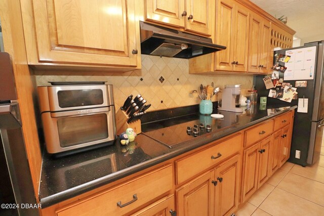 kitchen with decorative backsplash, black electric stovetop, light tile patterned flooring, and stainless steel refrigerator