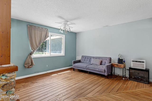 living room featuring light hardwood / wood-style floors, ceiling fan, a textured ceiling, and a wall mounted air conditioner