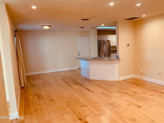 interior space featuring light wood-type flooring, kitchen peninsula, stainless steel refrigerator, and white cabinets