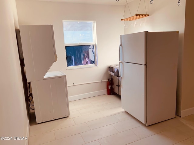 kitchen with light tile patterned floors, white fridge, and stacked washer / dryer