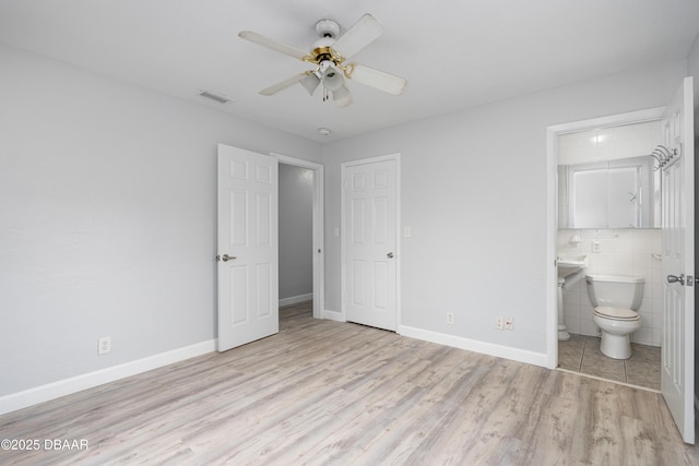 unfurnished bedroom with ceiling fan, ensuite bathroom, light hardwood / wood-style flooring, and tile walls