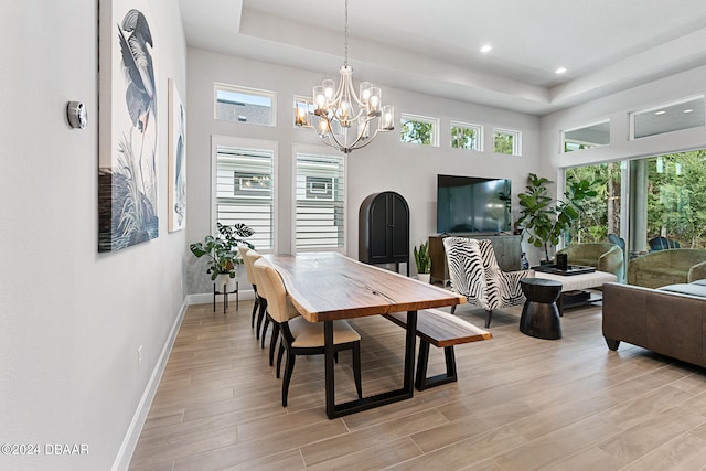 dining area featuring light hardwood / wood-style floors, a raised ceiling, and an inviting chandelier