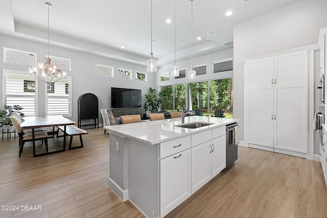 kitchen featuring a center island with sink, white cabinetry, light stone countertops, hanging light fixtures, and sink