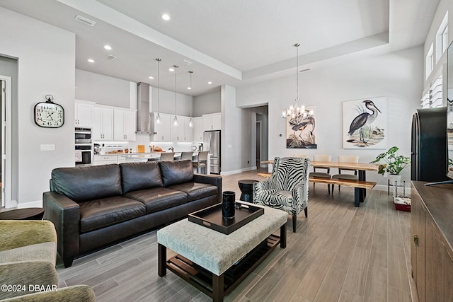 living room with light wood-type flooring, a tray ceiling, and an inviting chandelier