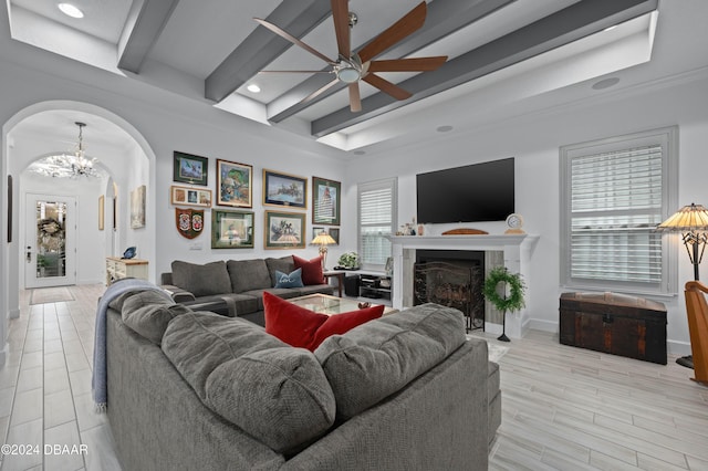 living area featuring arched walkways, a fireplace, beamed ceiling, baseboards, and ceiling fan with notable chandelier