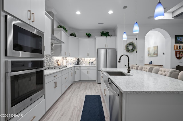 kitchen featuring white cabinetry, crown molding, an island with sink, and decorative light fixtures