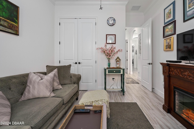 living room with visible vents, baseboards, light wood-type flooring, a glass covered fireplace, and crown molding