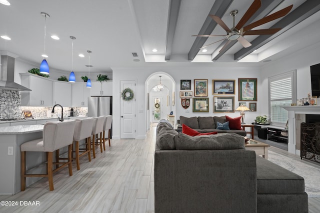 living area featuring arched walkways, light wood-style floors, a high end fireplace, ceiling fan, and beamed ceiling