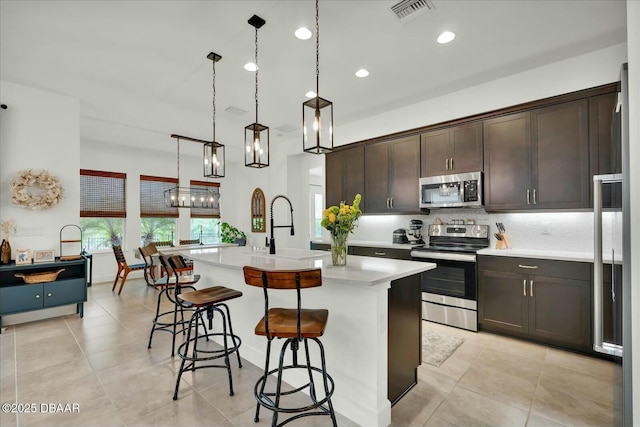 kitchen featuring visible vents, dark brown cabinetry, light countertops, a kitchen bar, and appliances with stainless steel finishes