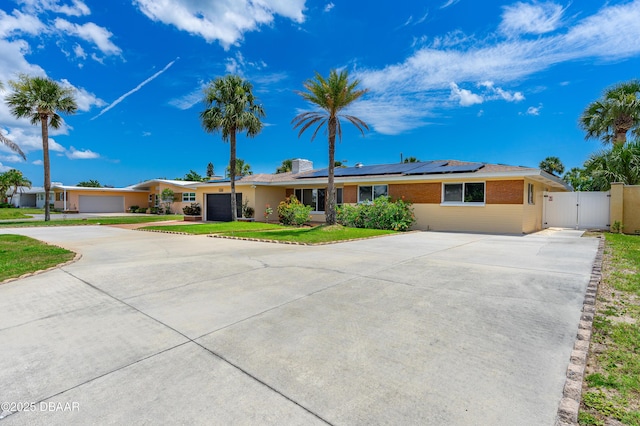 1104 Jacaranda Ave, Daytona Beach, FL 32118 - single story home with a gate, concrete driveway, roof mounted solar panels, and brick siding