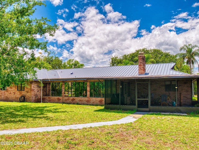 108 Dee St, New Smyrna Beach, FL 32168 - rear view of house featuring a lawn, a sunroom, a chimney, brick siding, and metal roof