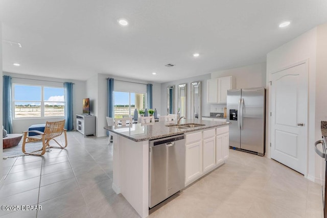 kitchen with sink, a center island with sink, appliances with stainless steel finishes, light stone countertops, and white cabinets