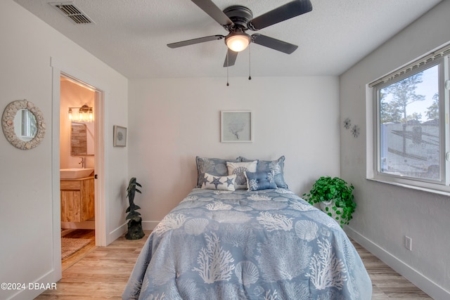 bedroom with a textured ceiling, light wood-type flooring, ensuite bath, and ceiling fan