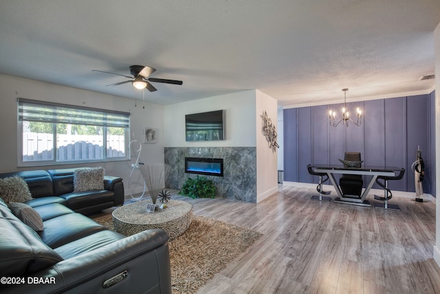 living room featuring ceiling fan with notable chandelier, light hardwood / wood-style floors, a premium fireplace, and a textured ceiling