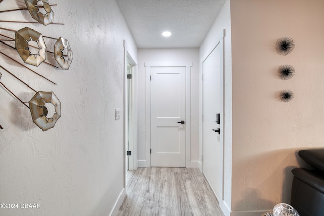 hall with a textured ceiling and light hardwood / wood-style flooring