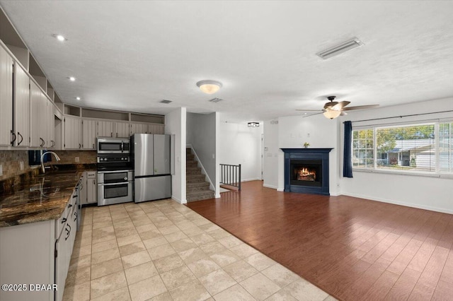 14 Woodlake Dr, Port Orange, FL 32129 - kitchen with appliances with stainless steel finishes, dark countertops, a sink, ceiling fan, and a lit fireplace