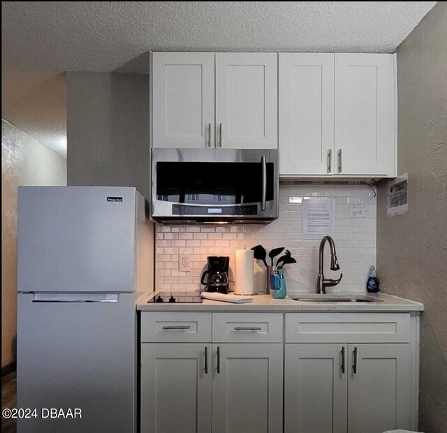 3501 S Atlantic Ave Unit 503, Daytona Beach, FL 32118 - kitchen featuring freestanding refrigerator, stainless steel microwave, a sink, a textured ceiling, and tasteful backsplash