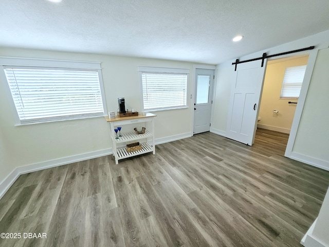 living area with a barn door, wood finished floors, a textured ceiling, baseboards, and recessed lighting