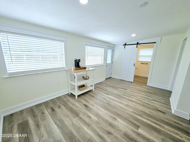 bedroom with a barn door, wood finished floors, a textured ceiling, baseboards, and recessed lighting