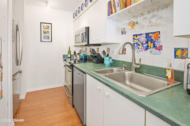 kitchen with backsplash, white cabinets, sink, light hardwood / wood-style flooring, and appliances with stainless steel finishes