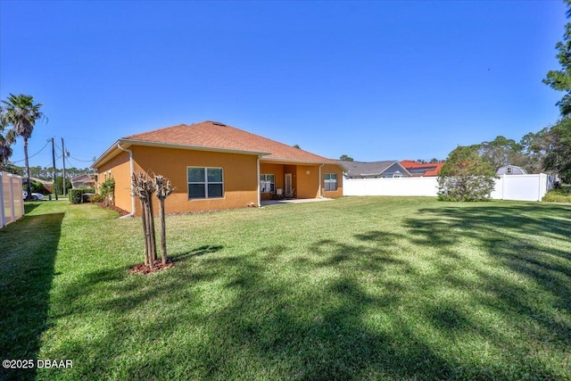 back of property with a lawn, fence, and stucco siding