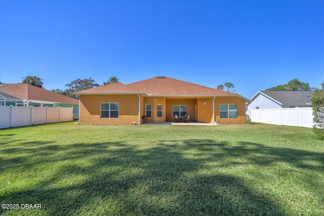 rear view of property featuring fence private yard, a lawn, and stucco siding