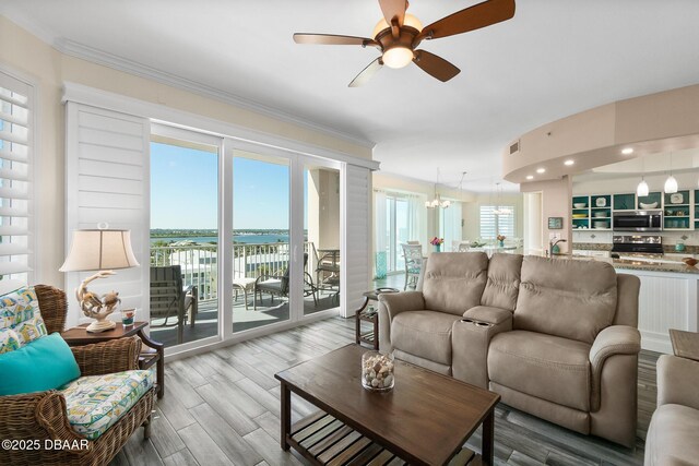 living room with ornamental molding, ceiling fan with notable chandelier, and wood-type flooring