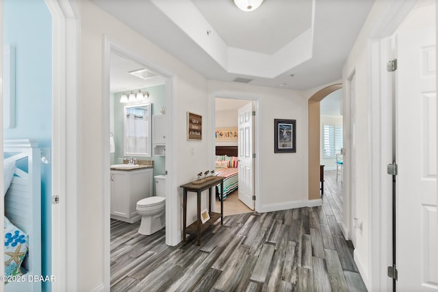 corridor with sink, dark hardwood / wood-style floors, and a tray ceiling