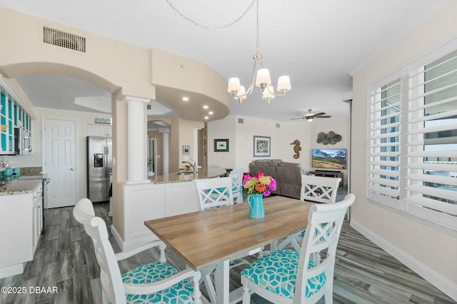 dining area featuring sink, decorative columns, ceiling fan with notable chandelier, and hardwood / wood-style flooring