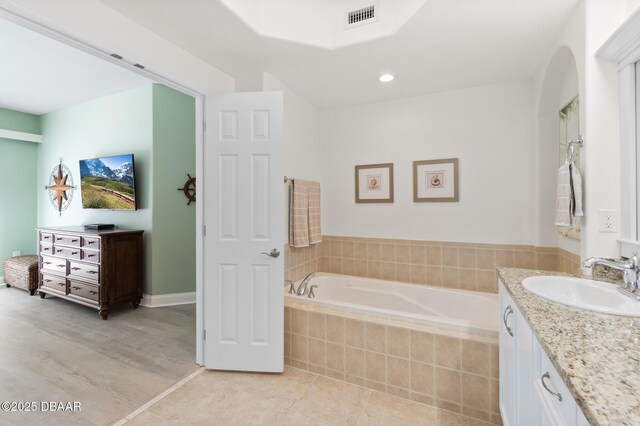 bathroom featuring tile patterned flooring, tiled bath, and vanity