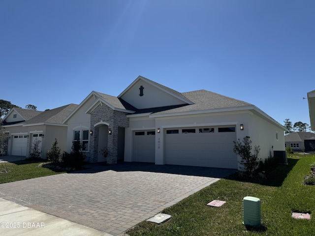 view of front of house featuring cooling unit, an attached garage, stucco siding, a front lawn, and decorative driveway