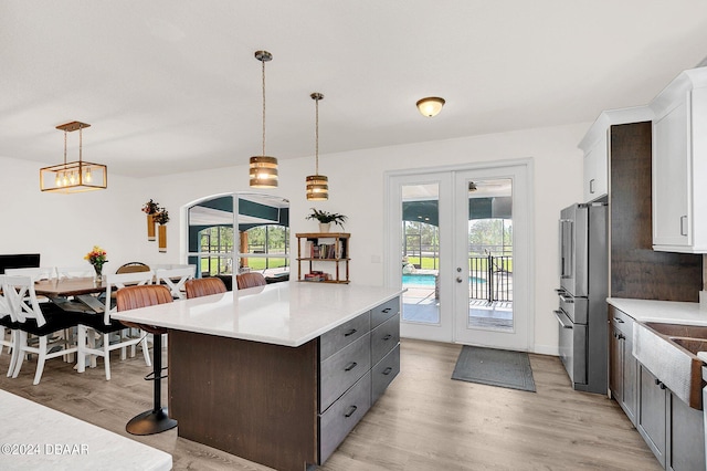 kitchen with a kitchen bar, french doors, light hardwood / wood-style floors, a center island, and hanging light fixtures