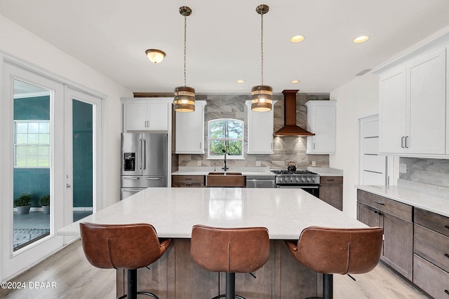 kitchen with appliances with stainless steel finishes, decorative light fixtures, decorative backsplash, sink, and wall chimney exhaust hood