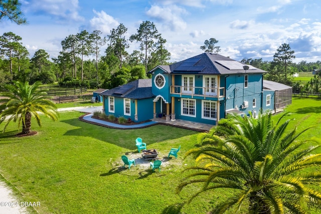 rear view of house with a patio, solar panels, a yard, a fire pit, and a balcony