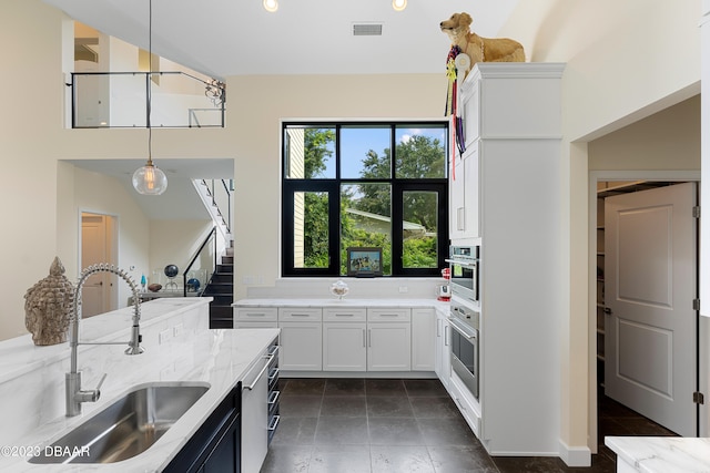 kitchen with hanging light fixtures, sink, light stone counters, and white cabinets