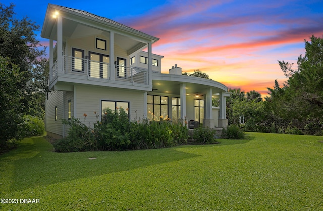 back house at dusk with a lawn and a balcony