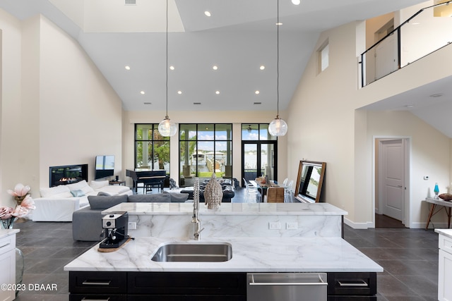 kitchen with white cabinets, a kitchen island with sink, high vaulted ceiling, light stone countertops, and pendant lighting