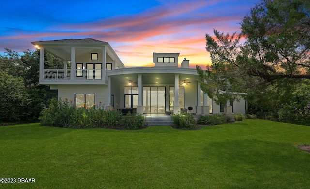 back house at dusk with a balcony and a yard