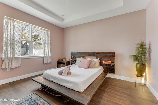 bedroom with baseboards, a raised ceiling, and wood finished floors